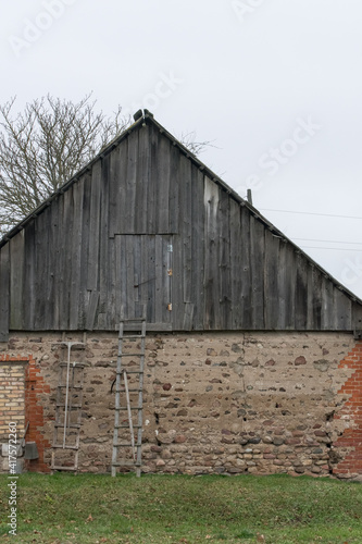 An old wooden shed with stairs and rakes during a cloudy day. Countryside view.