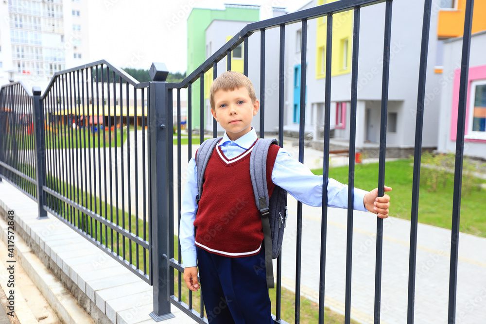 A boy in a school uniform with a backpack on his shoulders goes to school.