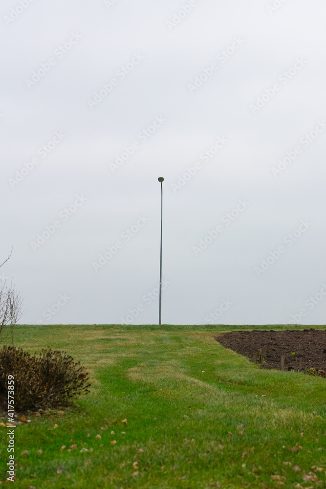 A lone light pole with grass in the foreground and a depressed day.