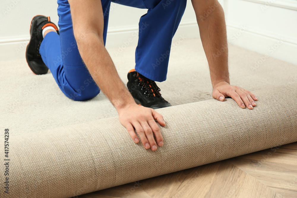 Naklejka premium Worker rolling out new carpet flooring indoors, closeup
