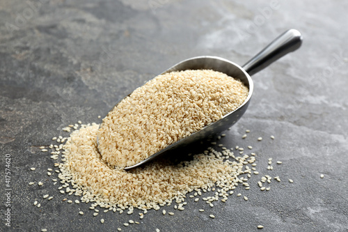 Metal scoop with white sesame seeds on grey table photo