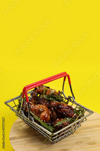 Wallpaper Mural Fresh cooked delicious chicken wings with green arugula in a metal shopping basket isolated on a yellow background. Food delivery. Torontodigital.ca
