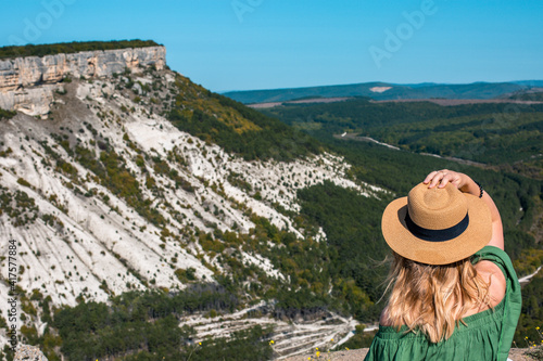 A girl in a hat sits and looks at the view from the observation deck in Chufut-Kale. Bakhchisarai, Crimea.