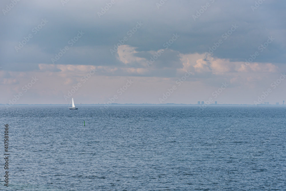 A lone sailing boat at sea off Malmo in the Oresund Strait with Copenhagen skyline and a cloudy sky suggests relaxation or break in calm water. Sailboat in the ocean conveys tranquillity and serenity