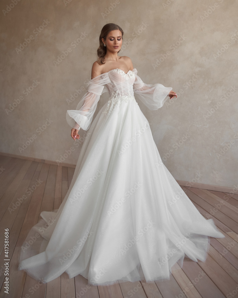 Full length bride portrait. Elegant woman in white wedding dress spinning in beige interior. Dynamic shot. Elegant female model standing and posing in ball gown Full length bride portrait. Elegant woman in white wedding dress spinning in beige interior. Dynamic shot. Elegant female model standing and posing in ball gown