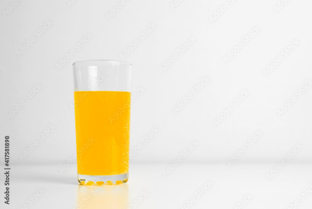 Glass of carbonated juice standing on table indoors. Light background, copy space Glass of carbonated juice standing on table indoors. Light background, copy space