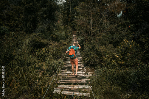 Podróżnik idący przez drewniany most wiszący przez dżunglę.