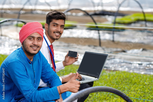 Young indian agronomist showing some information to farmer in laptop at greenhouse © PRASANNAPIX