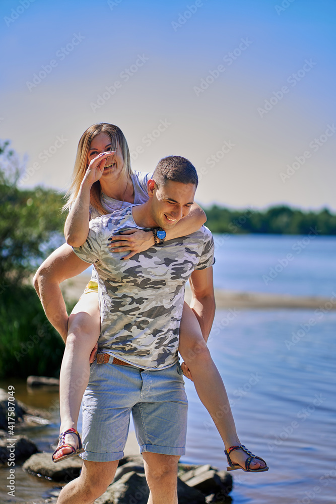 The man carries his girlfriend on his back across the stream. The woman laughs merrily. vertical The man carries his girlfriend on his back across the stream. The woman laughs merrily. vertical