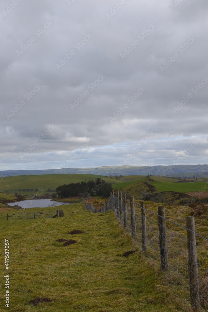 a long barbed wire fence sloping up a hill with a view of the welsh countryside behind it