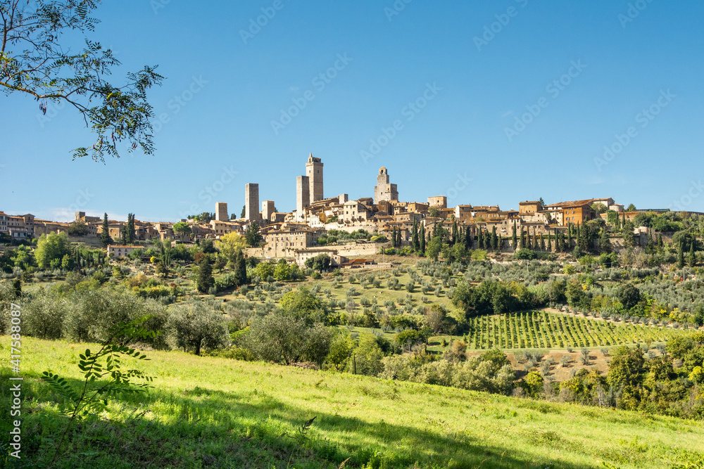 Panoramic view of San Gimignano, Tuscany., with olive orchards  and cypress trees under a blue sky