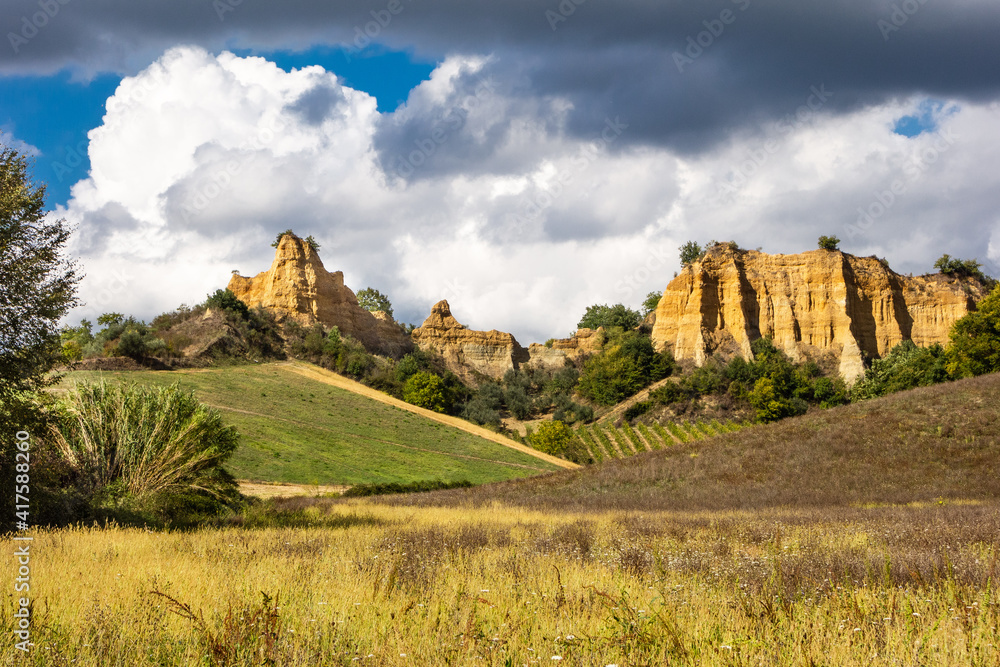Le Balze near Castelfranco, steep yellow rock cliffs against dark clouds with a meadow and a vineyard in the foreground