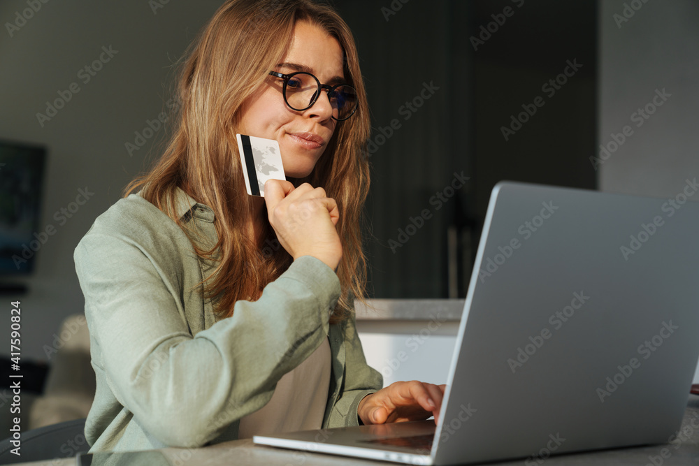 Brooding nice woman holding credit card and working with laptop Brooding nice woman holding credit card and working with laptop