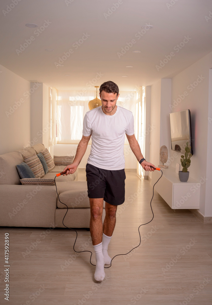 handsome young man doing exercises at home with jump rope during quarantine handsome young man doing exercises at home with jump rope during quarantine