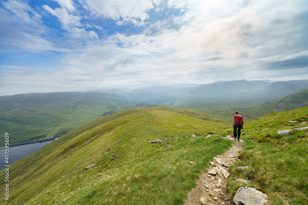 A hiker walking down from Creag an Fheadain towards Loch Daimh in the Scottish Highlands, UK mountain landscapes. A hiker walking down from Creag an Fheadain towards Loch Daimh in the Scottish Highlands, UK mountain landscapes.