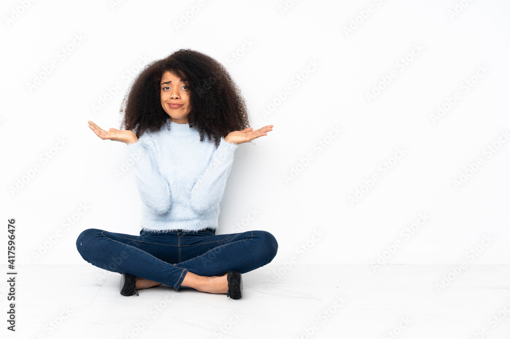 Young african american woman sitting on the floor having doubts while raising hands Young african american woman sitting on the floor having doubts while raising hands