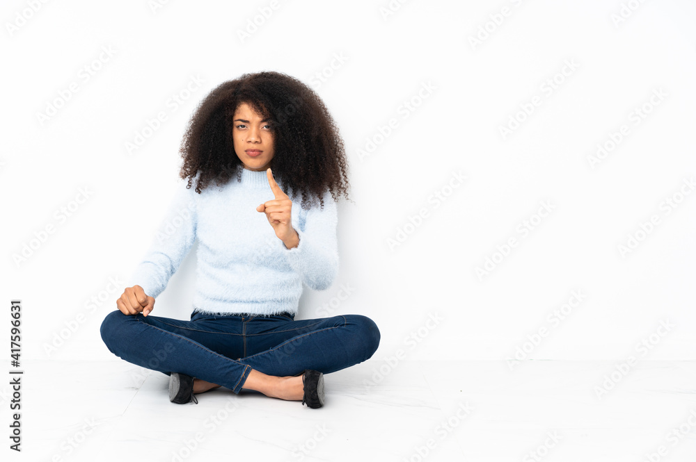 Young african american woman sitting on the floor frustrated and pointing to the front Young african american woman sitting on the floor frustrated and pointing to the front