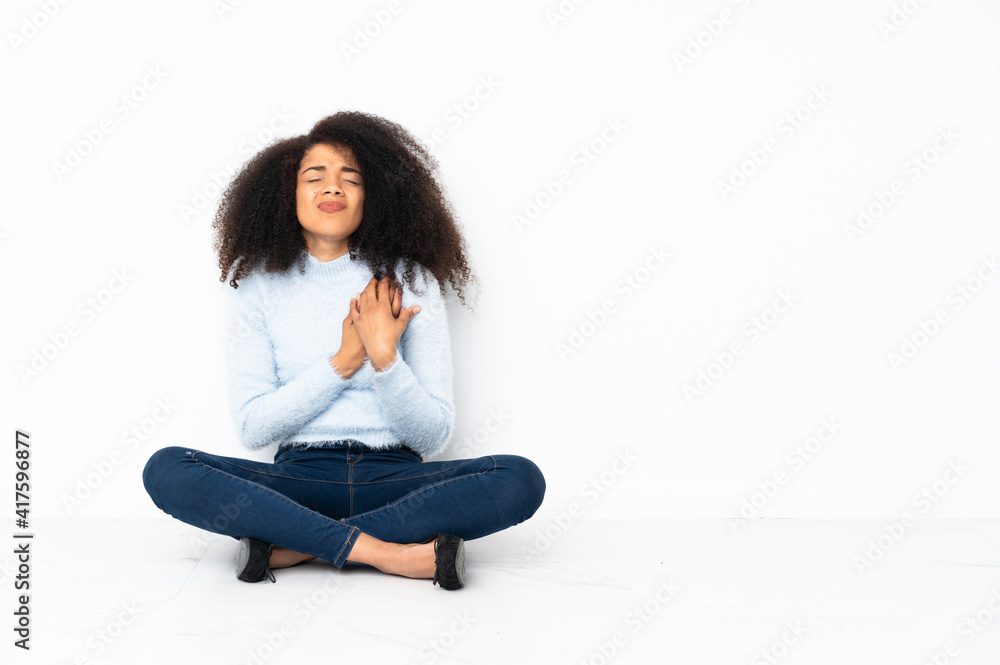 Young african american woman sitting on the floor having a pain in the heart Young african american woman sitting on the floor having a pain in the heart