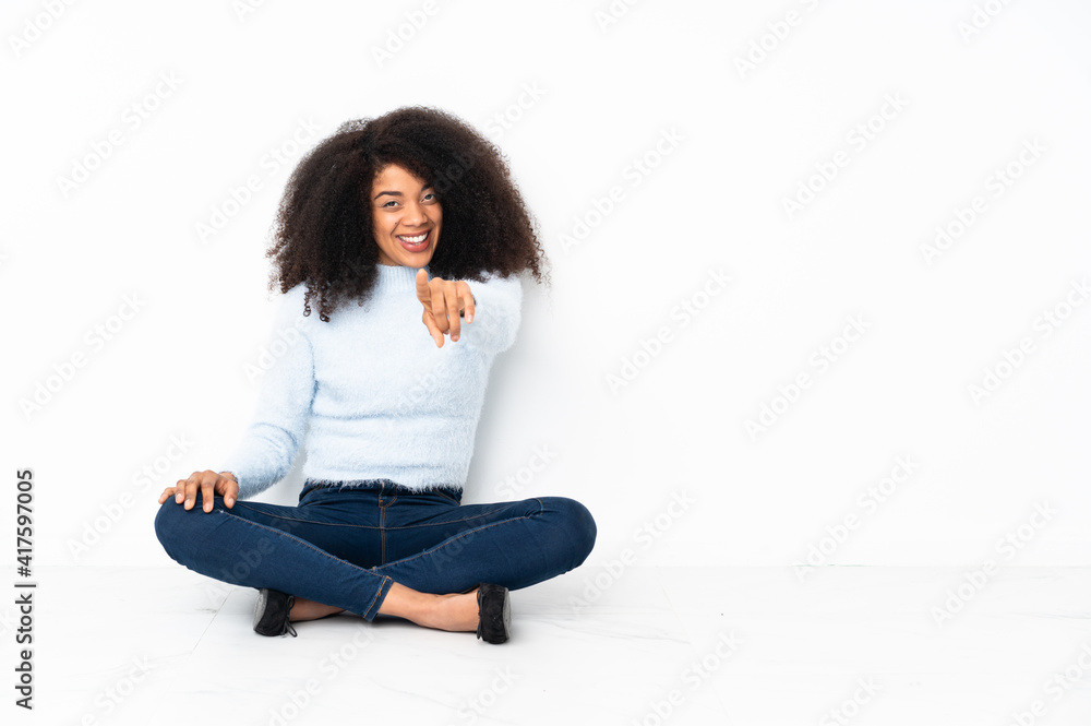 Young african american woman sitting on the floor points finger at you with a confident expression Young african american woman sitting on the floor points finger at you with a confident expression
