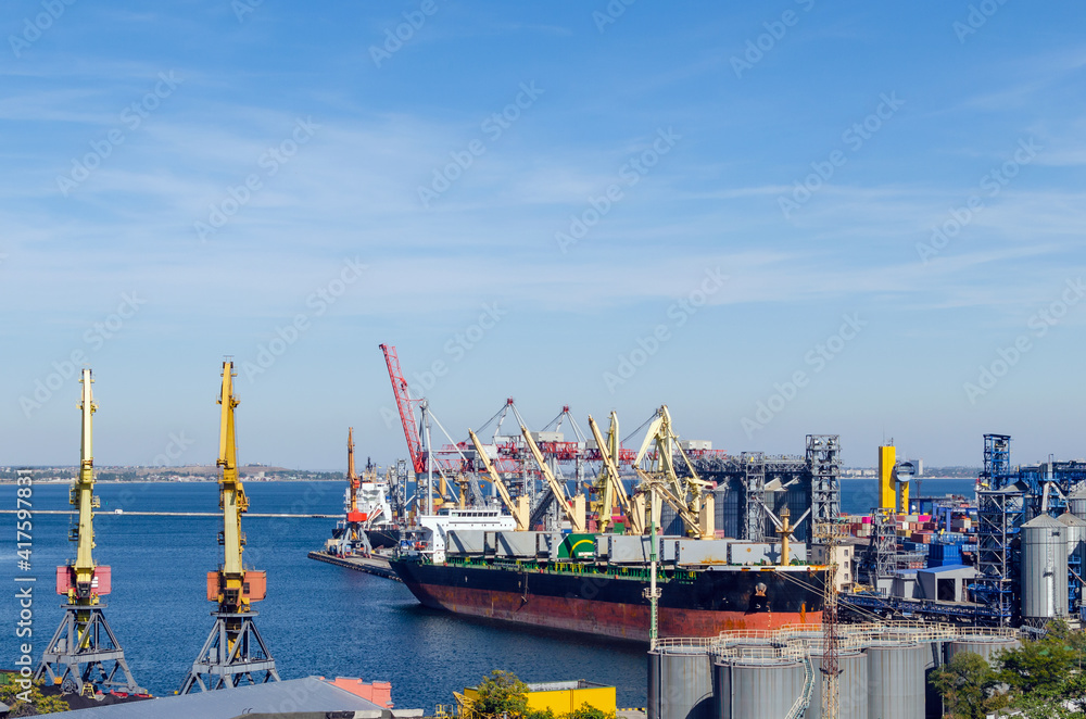 Fototapeta premium Port cargo crane loads a container onto a cargo ship in a seaport