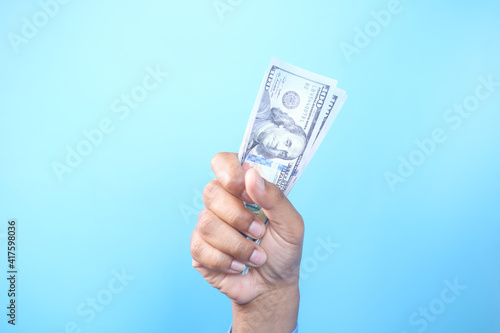 holding 100 us dollar cash in hand against blue background 