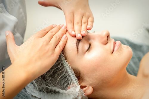 Young caucasian woman receiving facial massage by beautician s hands in spa medical salon
