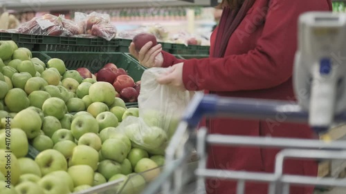 Girl in grocery store buys apples. She put the fruit in a bag. In the foreground is a cart with a validator for reading the barcode. Concept of healthy nutrition and vitamin intake