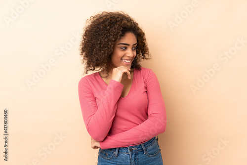 Young African American woman isolated on beige background looking to the side and smiling © luismolinero