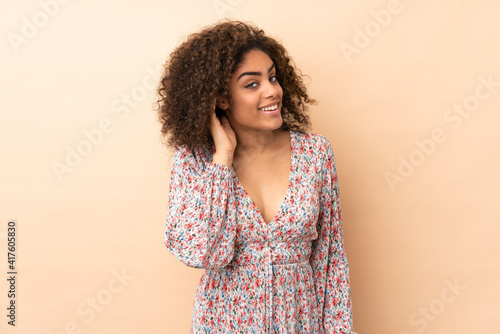 Young African American woman isolated on beige background listening to something by putting hand on the ear © luismolinero