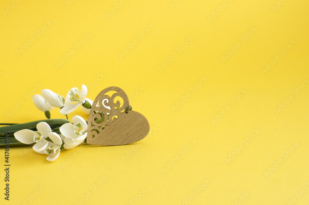 snowdrops, carved wooden heart on a yellow background snowdrops, carved wooden heart on a yellow background