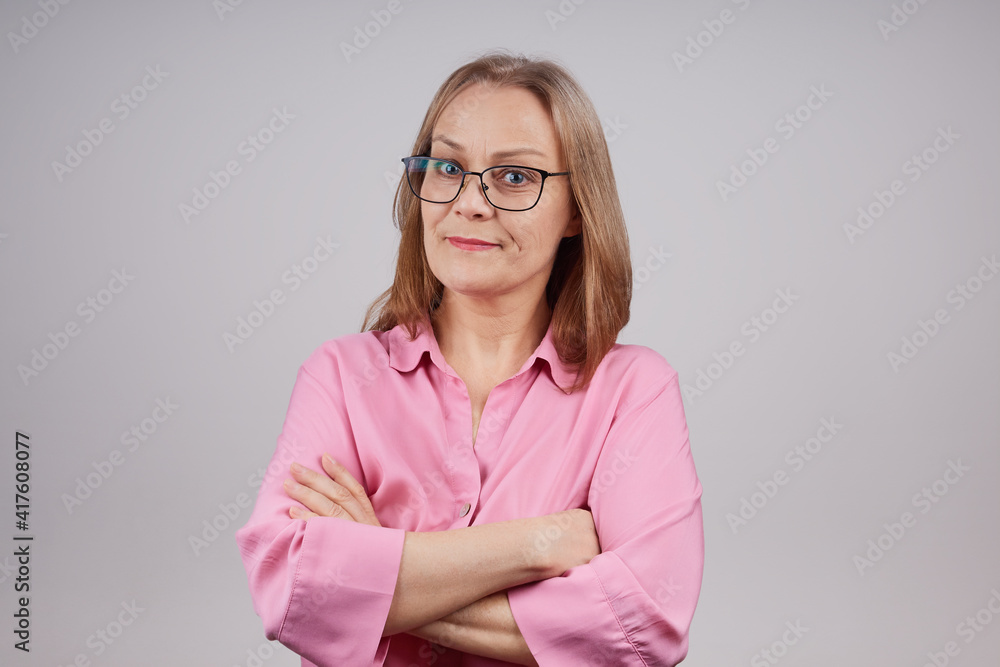Mature stylish business woman in glasses posing with folded arms on her chest, looking at the camera. Isolated shot on a gray background. Mature stylish business woman in glasses posing with folded arms on her chest, looking at the camera. Isolated shot on a gray background.