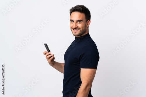 Young caucasian man using mobile phone isolated on white background smiling a lot © luismolinero