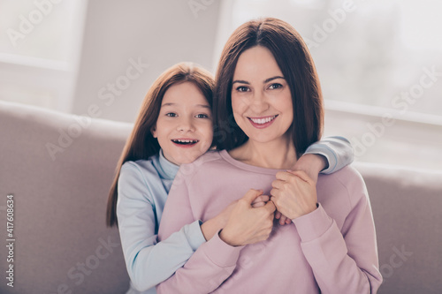 Photo of optimistic brunette red hairdo mom daughter hug play on sofa wear sweater at home