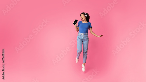 Happy asian woman singing using smartphone as mic