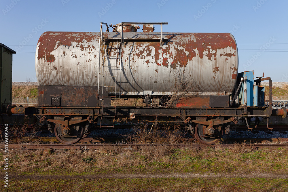 Naklejka premium Old train cistern tank wagon, rusty and weathered on abandoned train tracks in the field