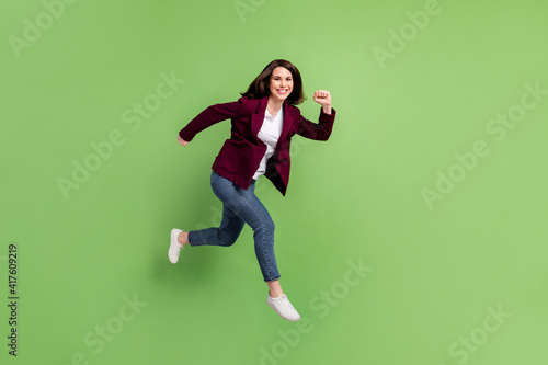 Full size profile photo of optimistic brown hairdo lady jump wear cardigan jeans sneakers isolated on green background