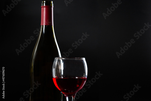 Wine bottle and glass with red wine on dark glossy background.