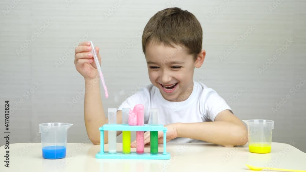 A happy child conducts experiments with chemicals by mixing them in a test tube. The boy laughs as he looks at the foam reaction in the test tube. The future of bioengineering, educational games for