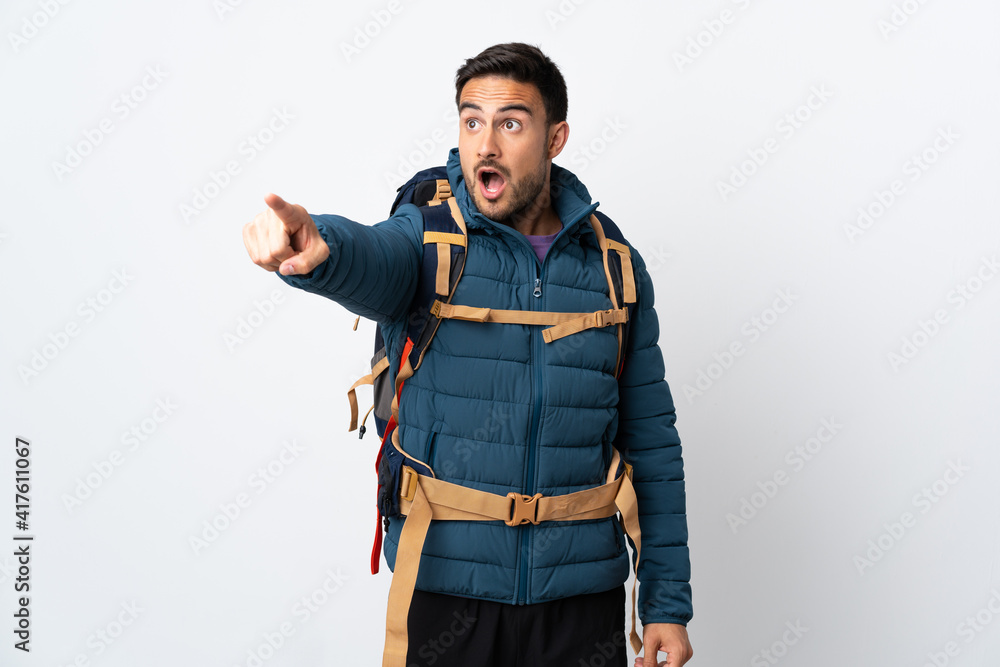 Young mountaineer man with a big backpack isolated on white background pointing away Young mountaineer man with a big backpack isolated on white background pointing away