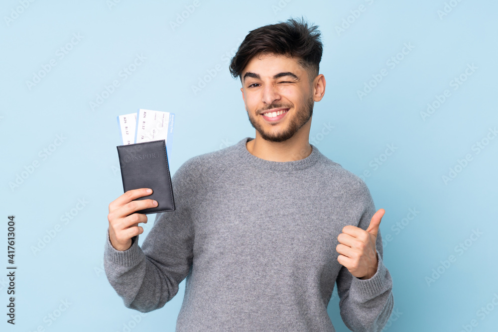 Arabian handsome man isolated on blue background in vacation holding a passport and plane with thumb up Arabian handsome man isolated on blue background in vacation holding a passport and plane with thumb up