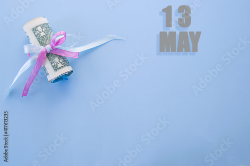 calendar date on blue background with rolled up dollar bills pinned by blue and pink ribbon with copy space. May 13 is the thirteenth day of the month