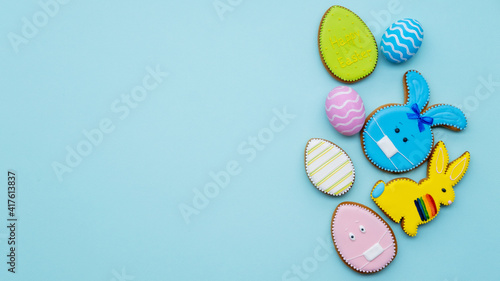 Pandemic banner. Happy Easter. Quarantine holiday celebration. Colorful gingerbread bunny cookie in protective face mask painted egg set with minimal design isolated on blue copy space background.