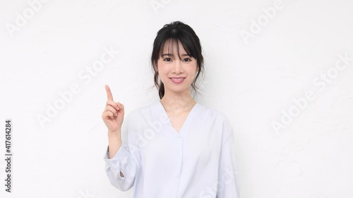 白い壁の前でポイントを示す若い女性