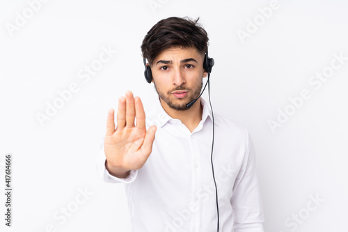 Telemarketer Arabian man working with a headset isolated on white background making stop gesture with her hand © luismolinero