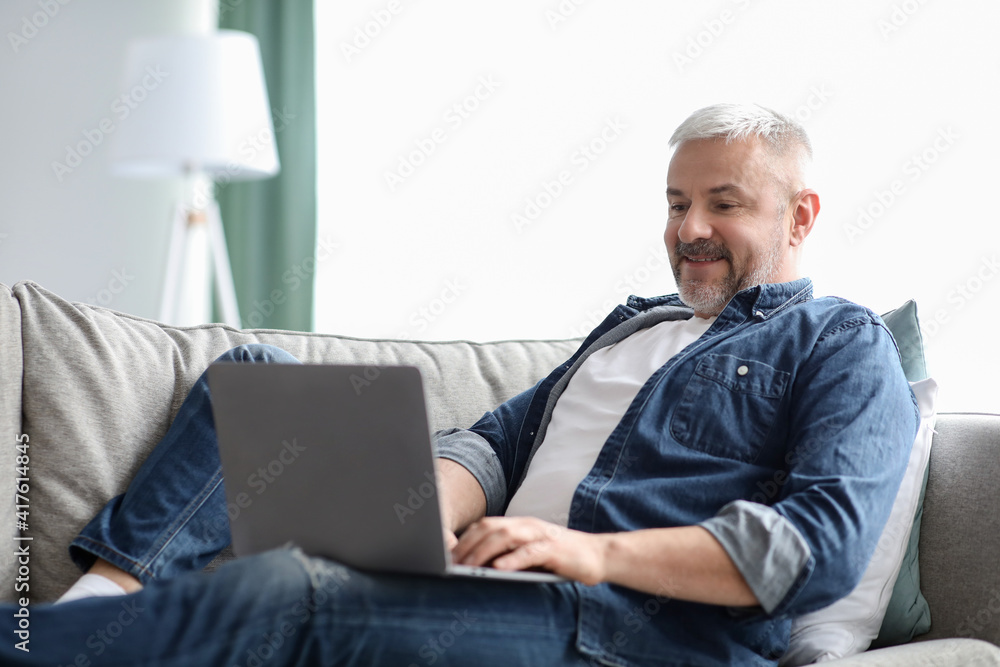 Happy mature man using laptop while resting on sofa Happy mature man using laptop while resting on sofa