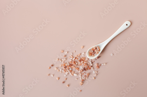 White ceramic spoon and scattered pink himalayan salt on a powder pink background. Copy space, top view. Healthy cooking, home care concept. Selective focus.