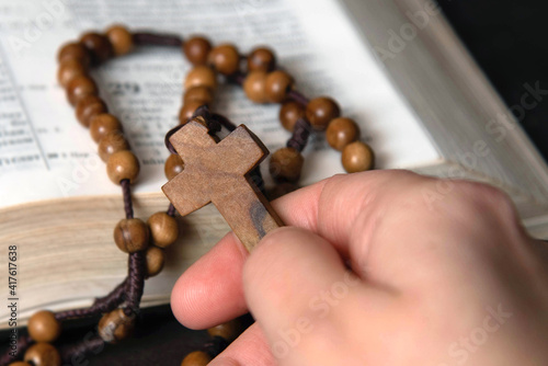 Woman holding and praying on rosary, on Bible background