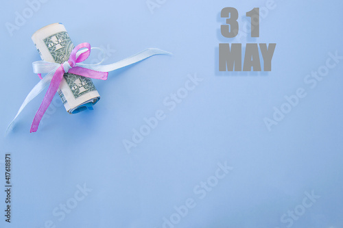 calendar date on blue background with rolled up dollar bills pinned by blue and pink ribbon with copy space. May 31 is the thirty-first day of the month