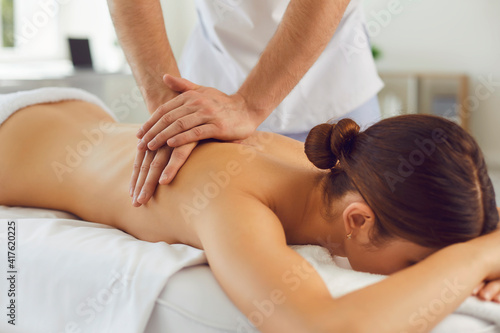 Young woman lying on massage table enjoying relaxing body massage done by professional masseur