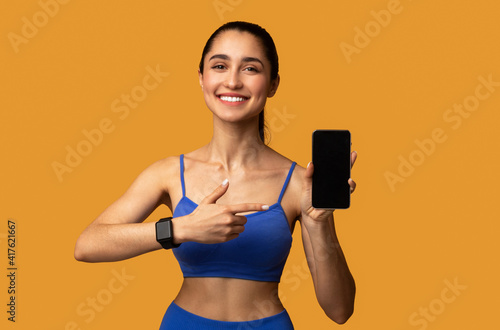 Happy sporty woman showing cellphone with black blank screen © Prostock-studio